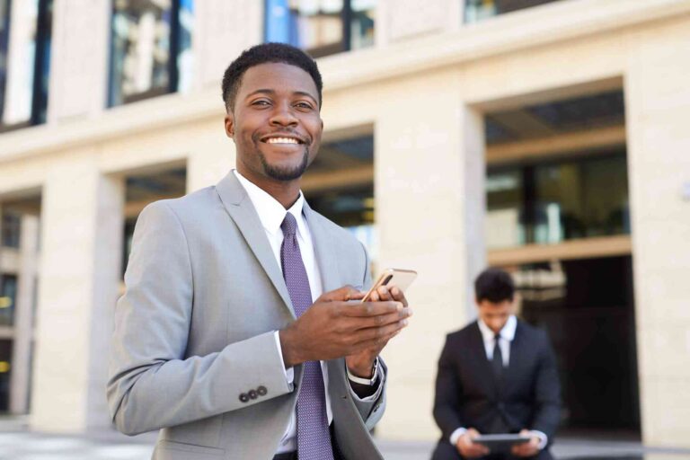 d670ad85192c4d7d90ba0002da60bc32-man-smiles-while-holding-phone-outside-of-a-building_l